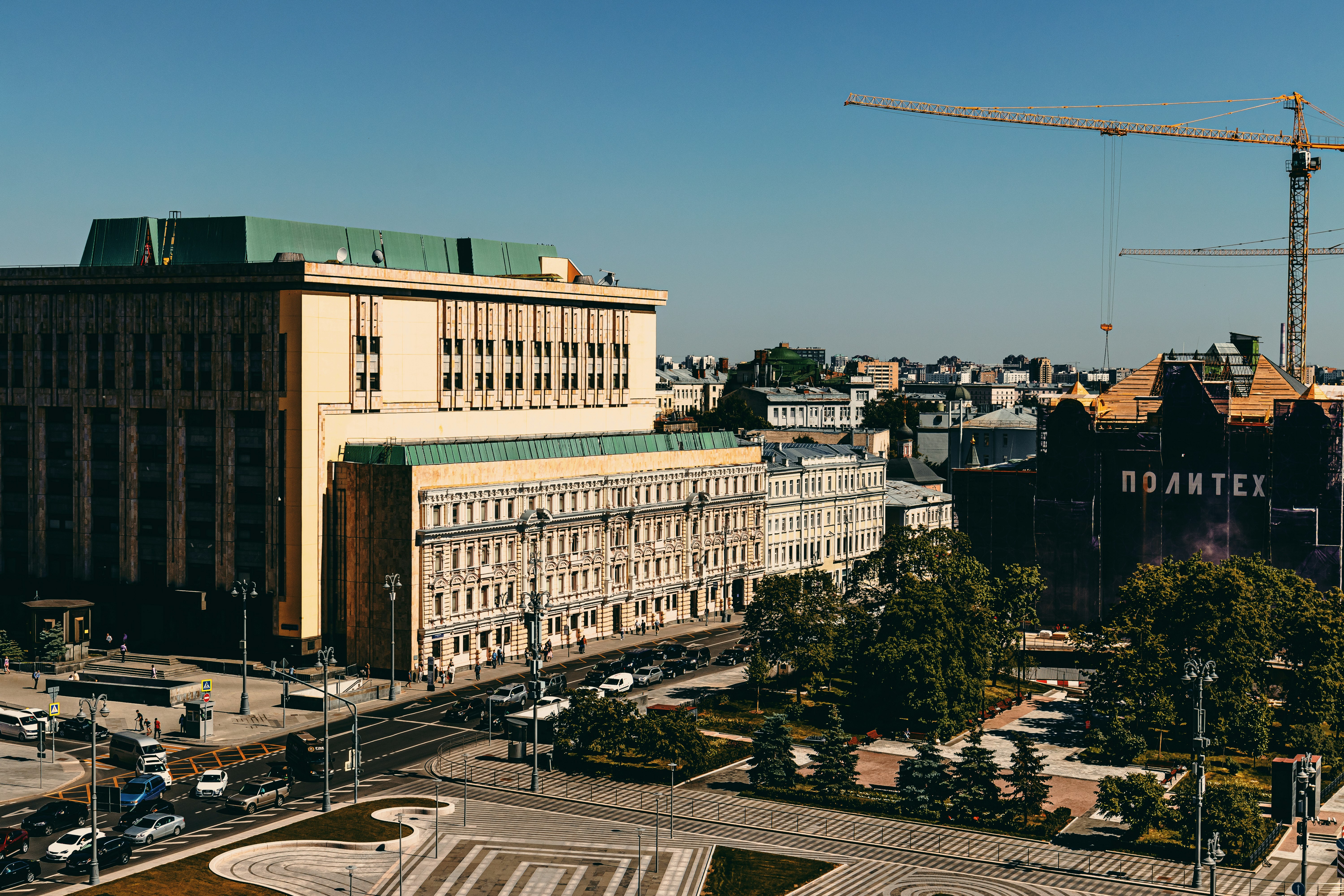 white and brown concrete building near green crane under blue sky during daytime